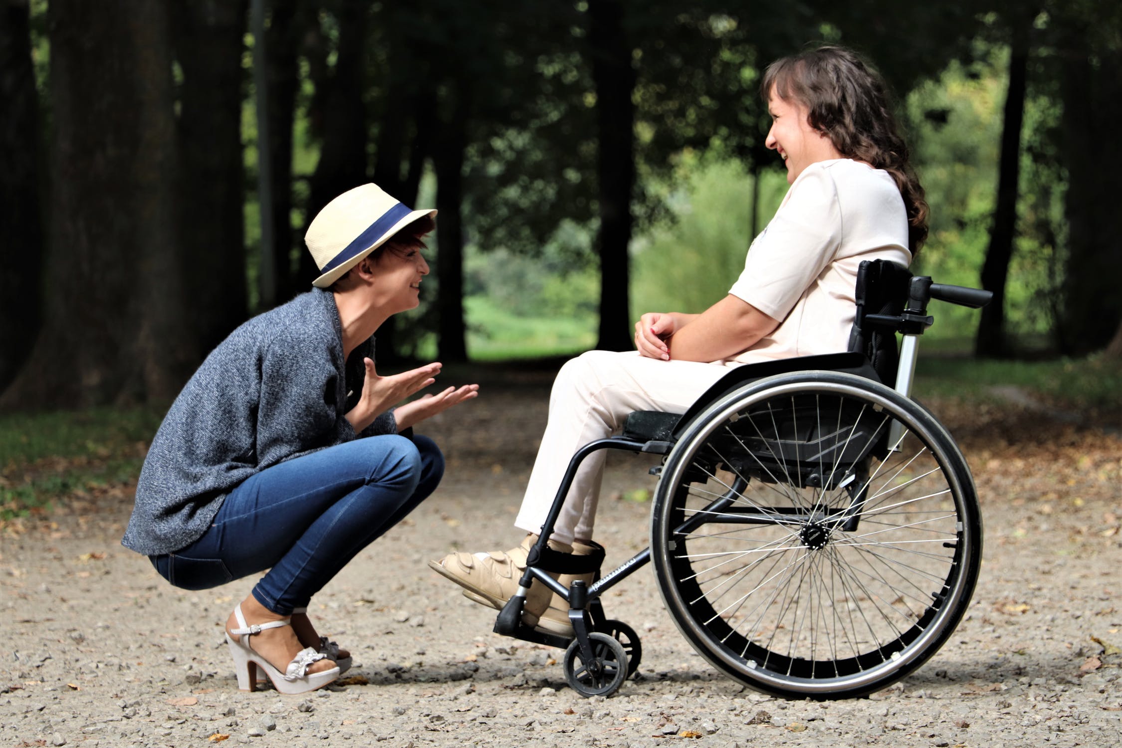 special needs trust, image of crouching woman laughing with another woman who is in a wheelchair